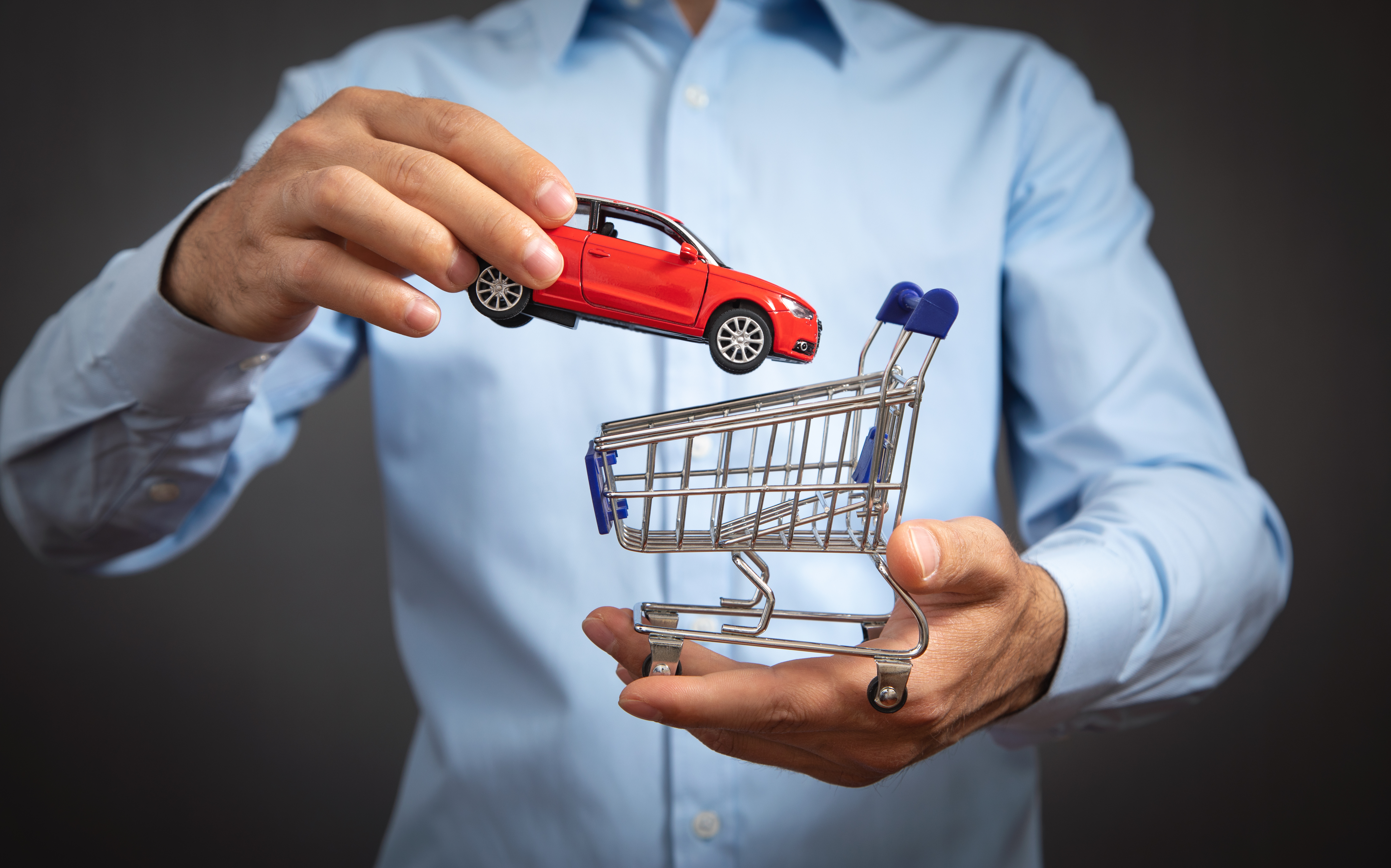 Businessman holding shopping cart and red toy car model.